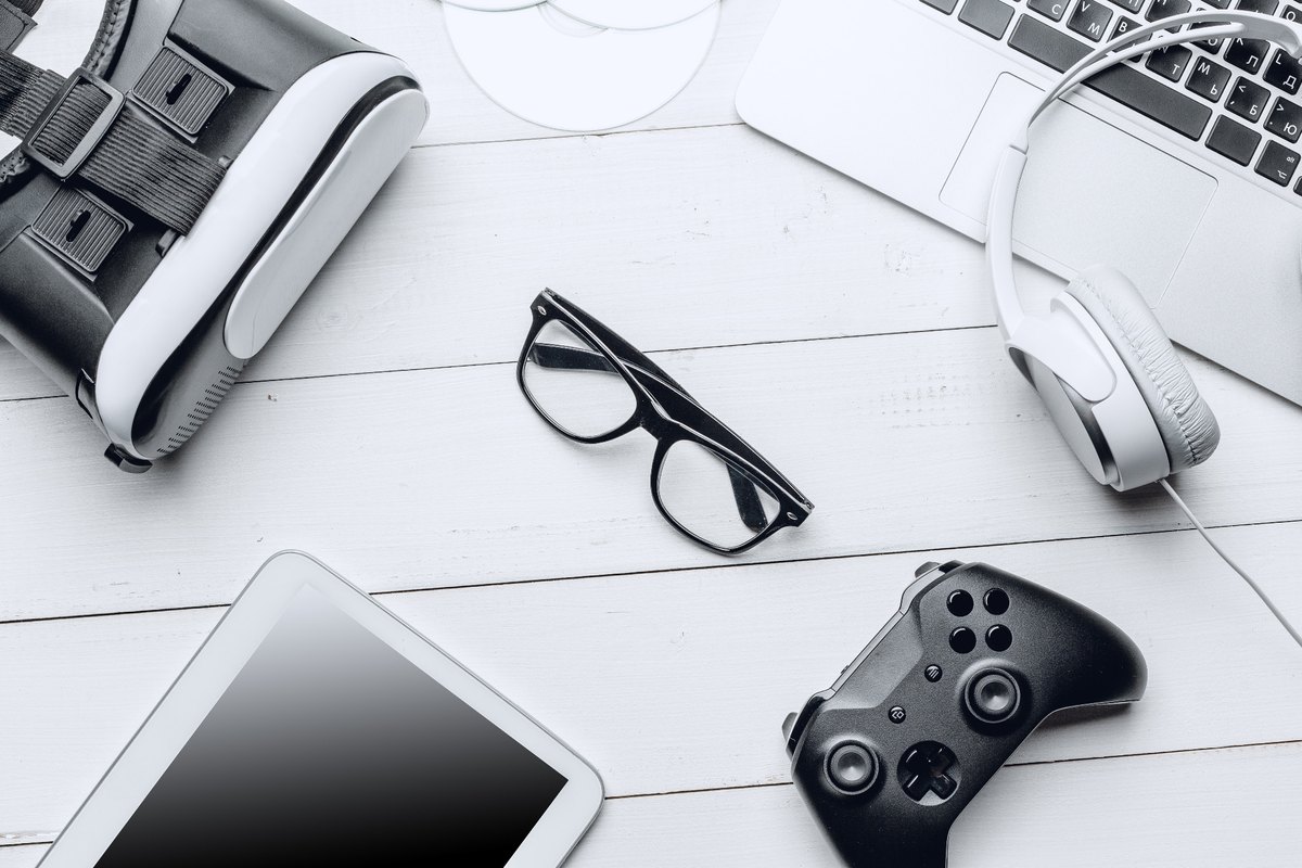 VR headset, laptop, headphones, tablet and game controller on a white desk